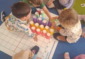 dzieci porządkują kubeczki kolorami przesuwając je po macie