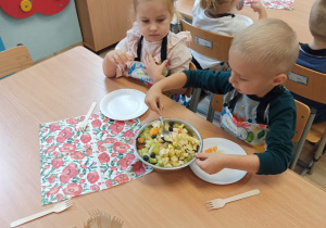 Dzieci zajadają sałatkę owocową.