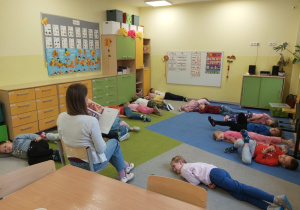 Grupa dzieci słucha ksiązki czytanej przez panią.