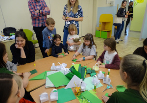 dzieci siedzą i skłądają żabki z origami