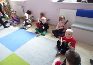 dzieci siedzą i grają na ukulele