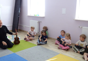 dzieci siedzą i trzymają ukulele