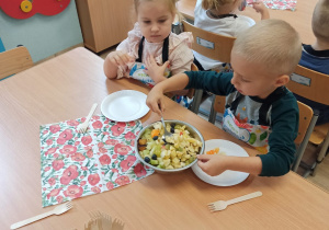 Dzieci zajadają sałatkę owocową.