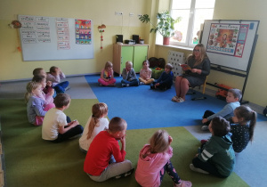 Dzieci siedzą w kręgu na dywanie.