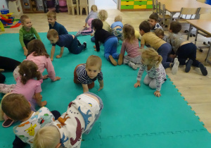 Dzieci czworakują na dywanie.