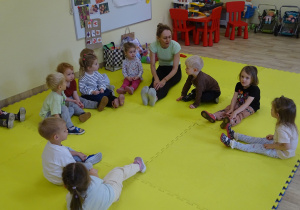 Dzieci siedzą na dywanie w siadzie prostym.