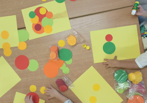 Dzieci wyklejają drzewo z kółek origami.