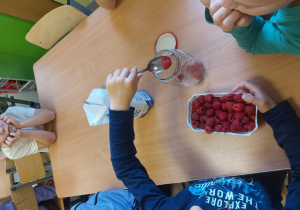 Dziecko wsypuje maliny do słoika.