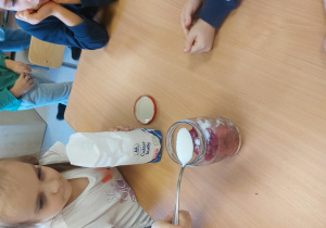 Dziewczynka wsypuje cukier do słoika.