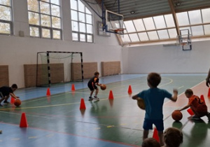 Chłopcy i dziewczynki pokonują tor przeszków kozłując piłkę