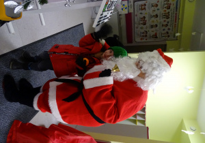 Święty Mikołaj i jego pomocnicy witają dzieci, które przyszły do przedszkola.