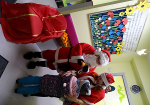 Święty Mikołaj i jego pomocnicy witają dzieci, które przyszły do przedszkola.