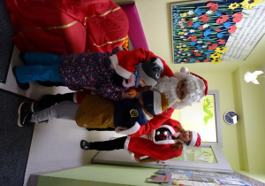 Święty Mikołaj i jego pomocnicy witają dzieci, które przyszły do przedszkola.