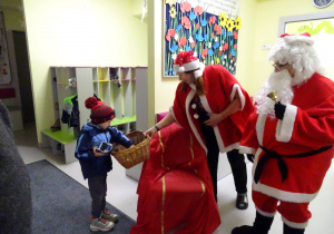 Święty Mikołaj i jego pomocnicy witają dzieci, które przyszły do przedszkola.