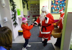Święty Mikołaj i jego pomocnicy witają dzieci, które przyszły do przedszkola.