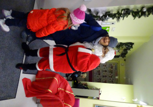 Święty Mikołaj i jego pomocnicy witają dzieci, które przyszły do przedszkola.