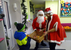 Święty Mikołaj i jego pomocnicy witają dzieci, które przyszły do przedszkola.