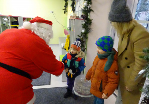 Święty Mikołaj i jego pomocnicy witają dzieci, które przyszły do przedszkola.