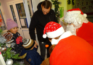 Święty Mikołaj i jego pomocnicy witają dzieci, które przyszły do przedszkola.