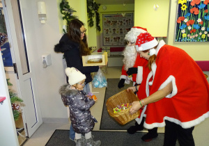 Święty Mikołaj i jego pomocnicy witają dzieci, które przyszły do przedszkola.