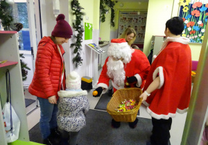 Święty Mikołaj i jego pomocnicy witają dzieci, które przyszły do przedszkola.