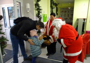 Święty Mikołaj i jego pomocnicy witają dzieci, które przyszły do przedszkola.