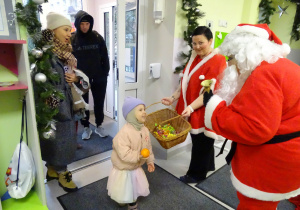 Święty Mikołaj i jego pomocnicy witają dzieci, które przyszły do przedszkola.