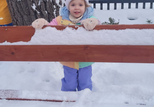 dziewczynka trzyma zaśnieżone oparcie ławki