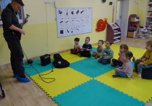 Dzieci słuchają gry na gitarze elektrycznej.
