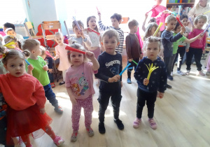 dzieci stoją i trzymają kolorowe papierowe miotełki