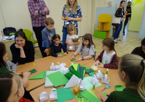 dzieci siedzą i skłądają żabki z origami