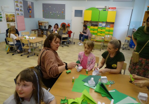 dzieci wraz z rodzicami składają koszyczki i żabki z papieru