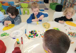 Dzieci siedzą przy stole i ozdabiają kartki