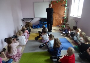 dzieci siedzą podzielone na trzy rzędy i grają na ukulele