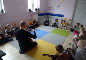dzieci siedzą i grają na ukulele