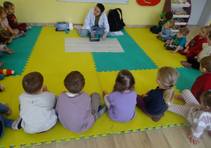 dzieci siedzą, słuchają i patrzą na prowadzącą zajęcia