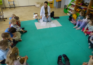 dzieci siedzą i słuchają prowadzącą zajęcia