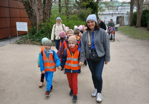 Dzieci razem z nauczycielem i opiekunami idą po alejce w parku