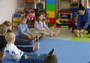Dzieci siedzą na dywanie i wykonują skłony