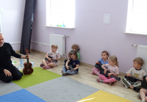 dzieci siedzą i trzymają ukulele