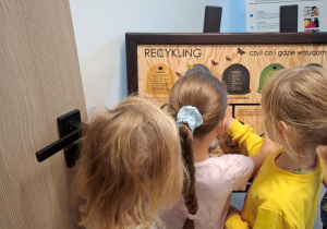 dziewczynki ogladają tablicę manipulacyjną na temat recyklingu